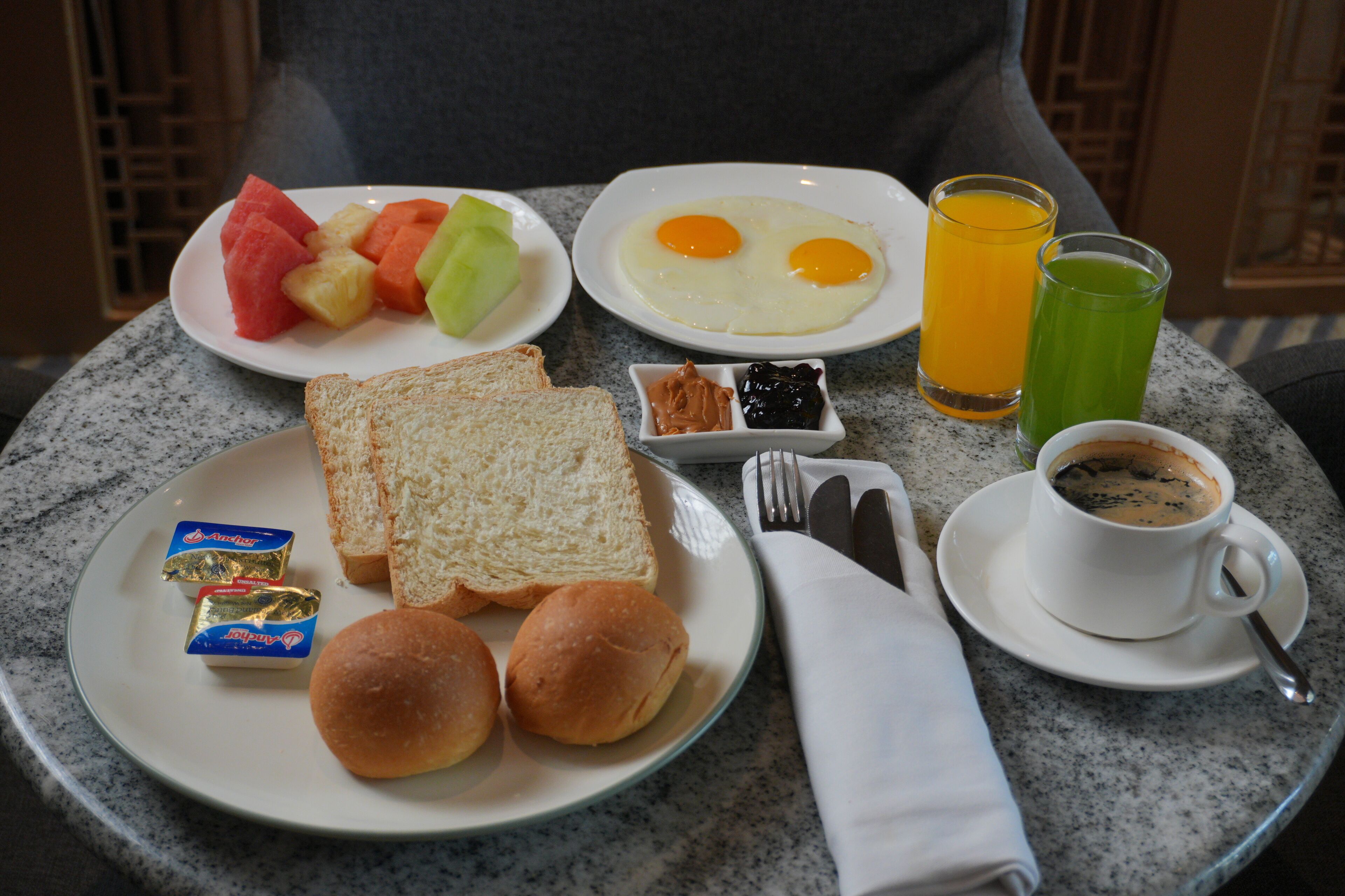 Un plateau de petit-déjeuner avec des toasts, des œufs, des fruits et des boissons, posé sur une table en marbre.