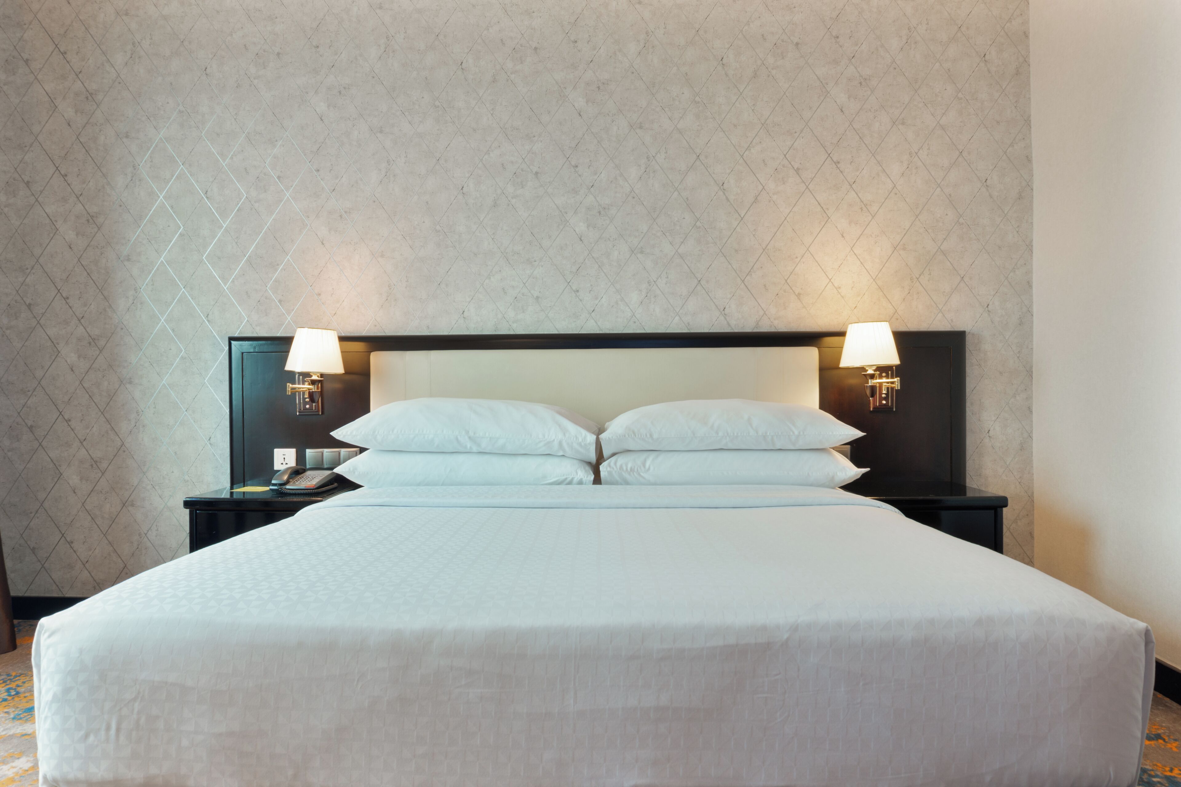 A hotel room with a large bed, two bedside tables with lamps, and a patterned wall.