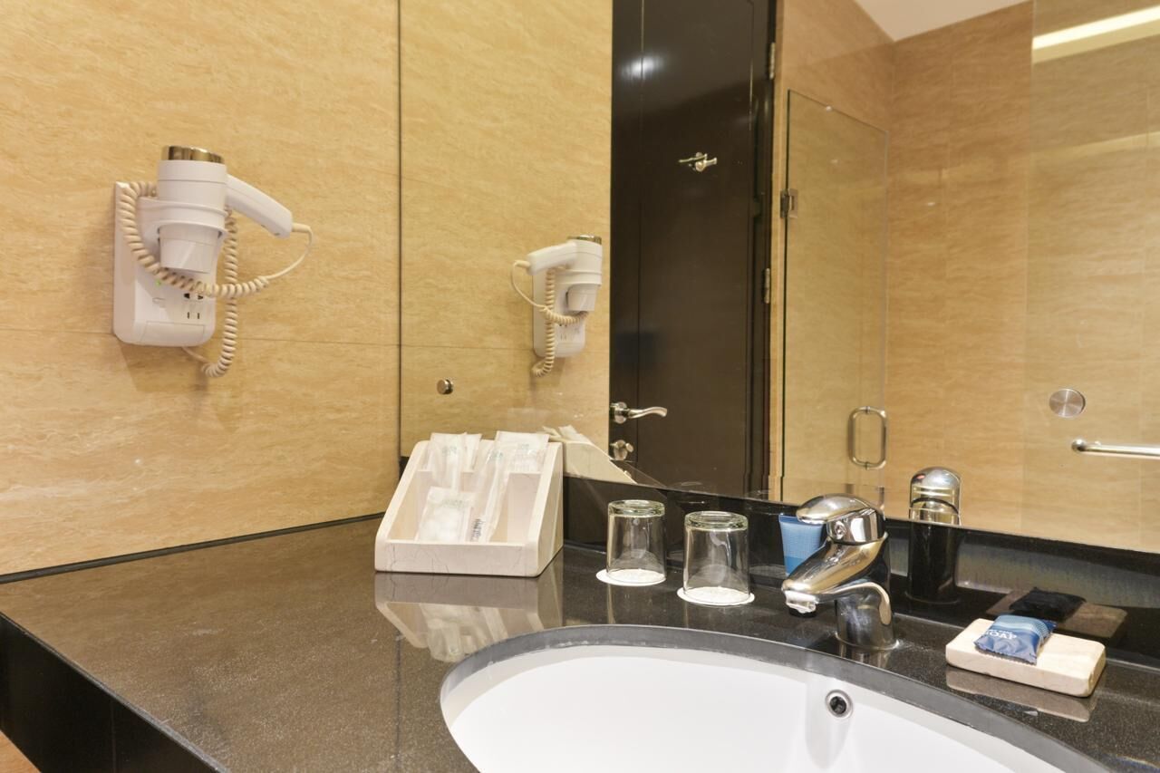 Un baño de hotel con lavamanos, espejo, secador de pelo y toallero.