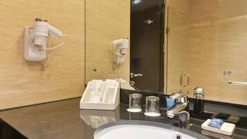 Un baño de hotel con lavamanos, espejo, secador de pelo y toallero.