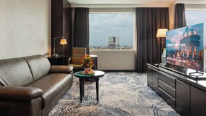 Habitación de hotel con sofá, una mesita con un jarrón de flores, televisión y vista a la ciudad.
