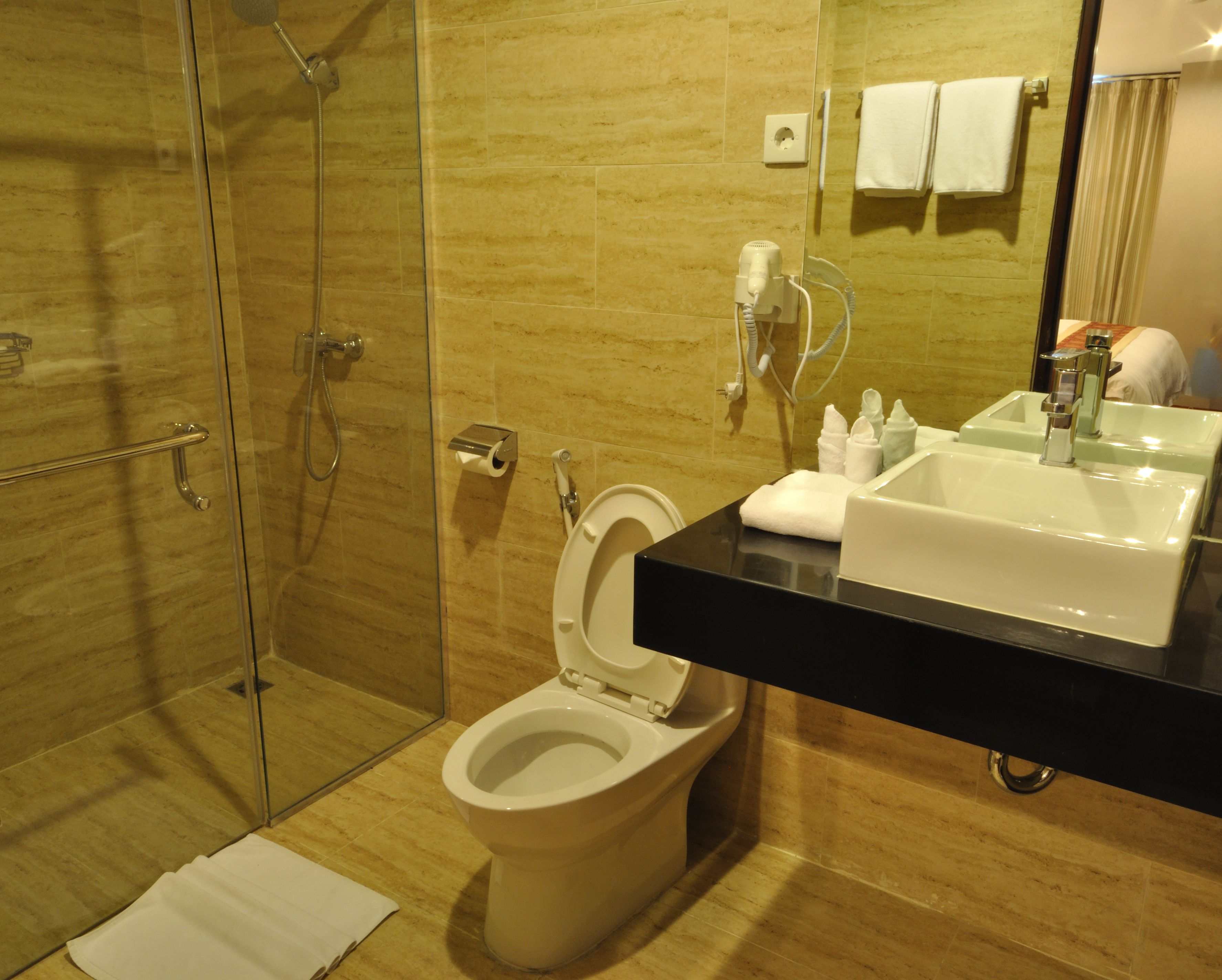 Um banheiro moderno com box de vidro, vaso sanitário, pia com bancada preta e espelho refletindo o ambiente.