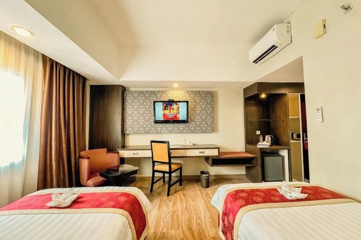 Una habitación de hotel con dos camas, un escritorio, una silla, un televisor y un minibar.