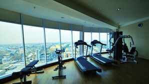 A gym with treadmills, a bench, and a rowing machine, featuring large windows with a city view.