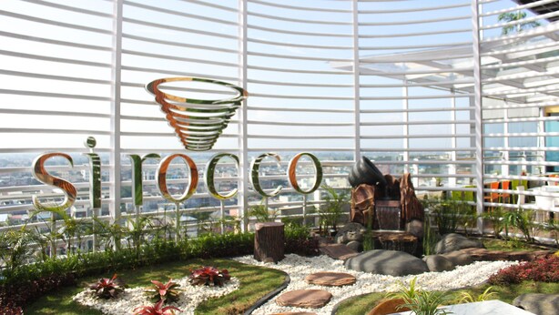 A modern indoor garden with a view of the city, featuring a unique name display and natural elements like rocks and plants.
