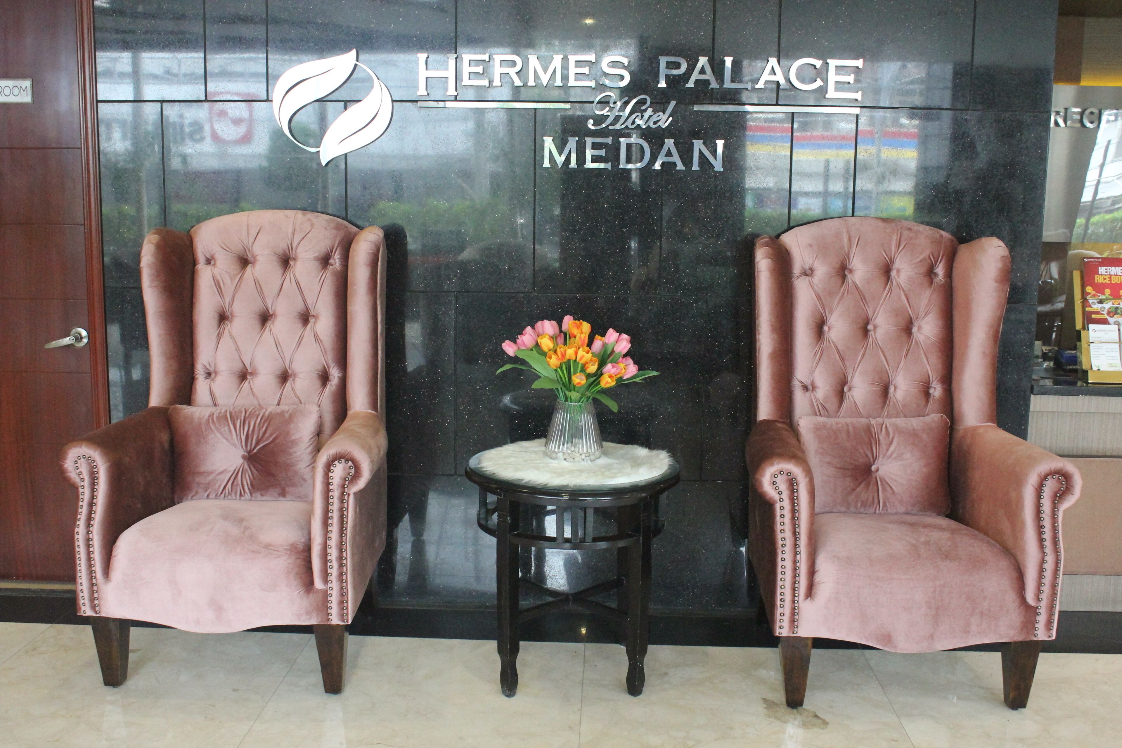 Two plush armchairs with a vase of flowers on a small table in front of a hotel sign.