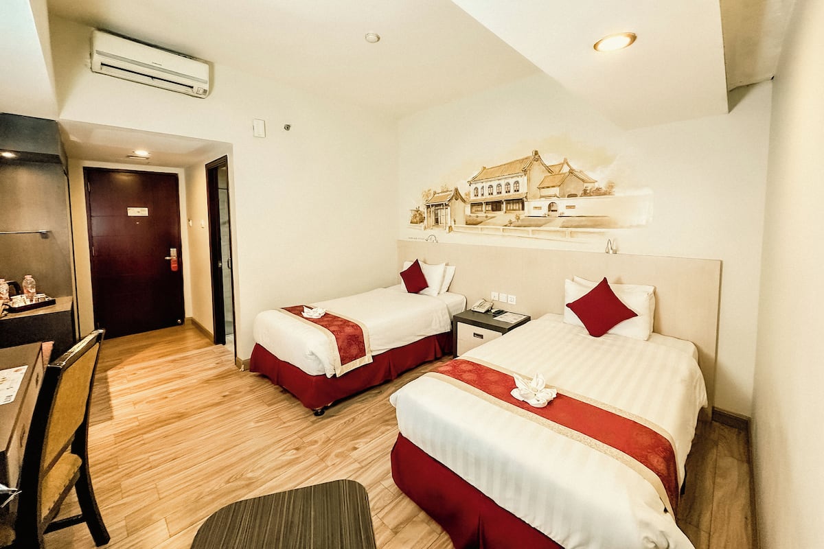 Ein Hotelzimmer mit zwei Betten, einem Schreibtisch und einer Klimaanlage.