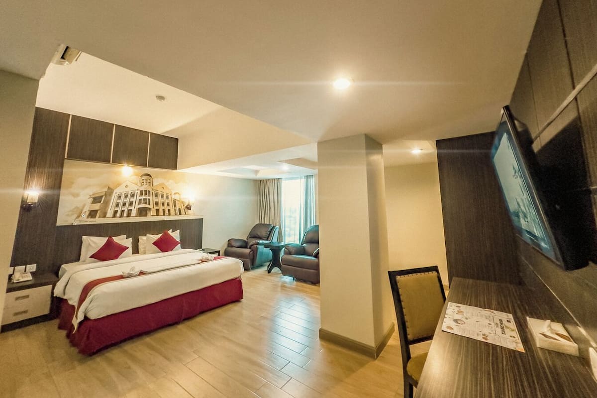 Ein Hotelzimmer mit Bett, zwei Stühlen, einem Schreibtisch und einem Fernseher.
