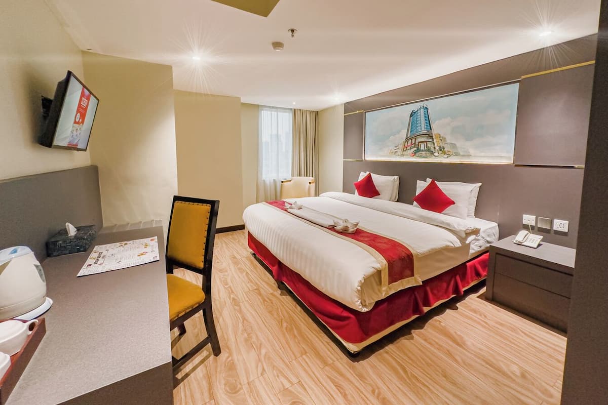 Ein Hotelzimmer mit einem großen Bett, einem Schreibtisch mit Stuhl, einem flachbildfernseher an der Wand und einem fenster mit Vorhängen.