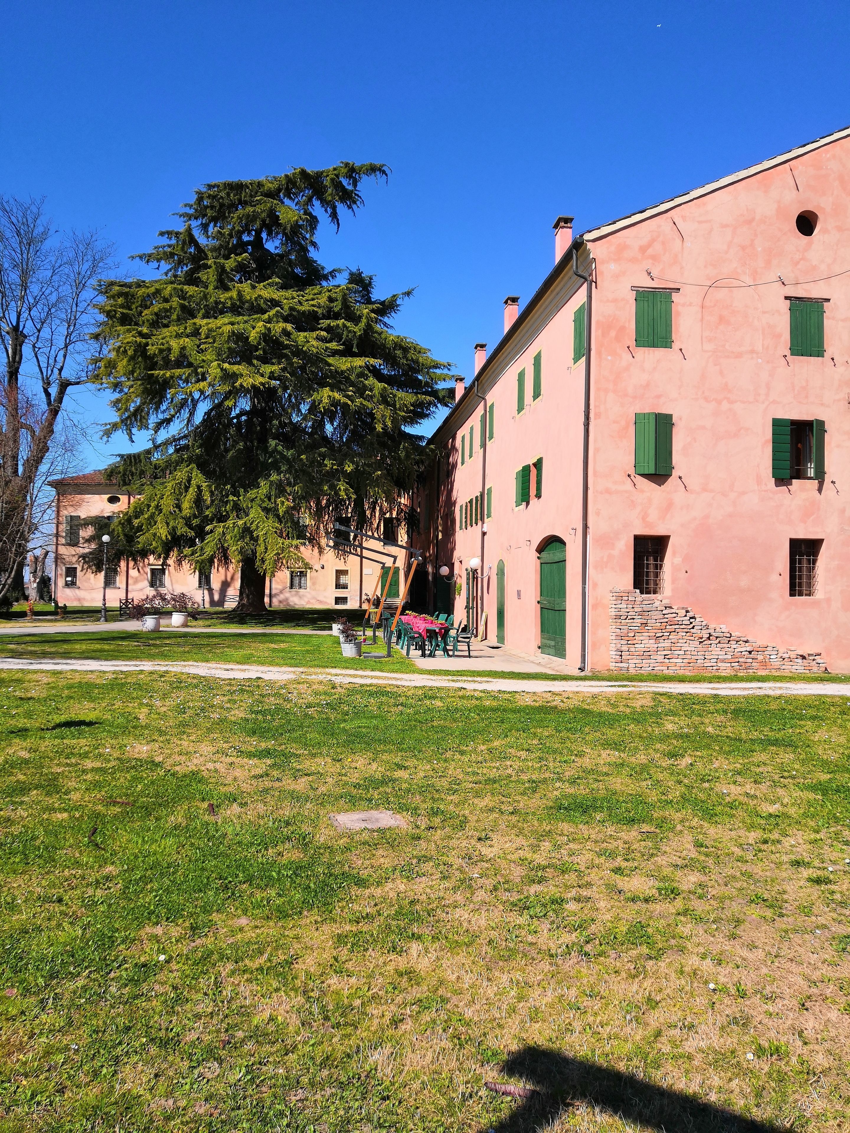 A building with a pink facade, green shutters, and a staircase leading to the entrance.