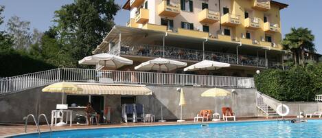 Un hotel con piscina, mobiliario exterior y balcón con sombrillas.