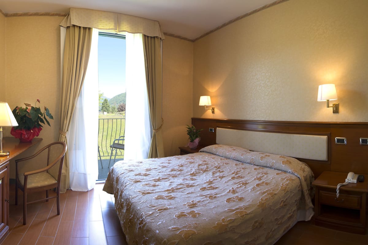 Een hotelkamer met een bed, nachtkastje, lamp, stoel en uitzicht op het omliggende landschap.