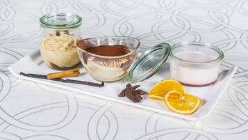 Tres frascos de vidrio con tapas sobre una bandeja blanca, conteniendo diferentes mezclas, acompañados de ramitas de canela, trozos de chocolate y rodajas de naranja.