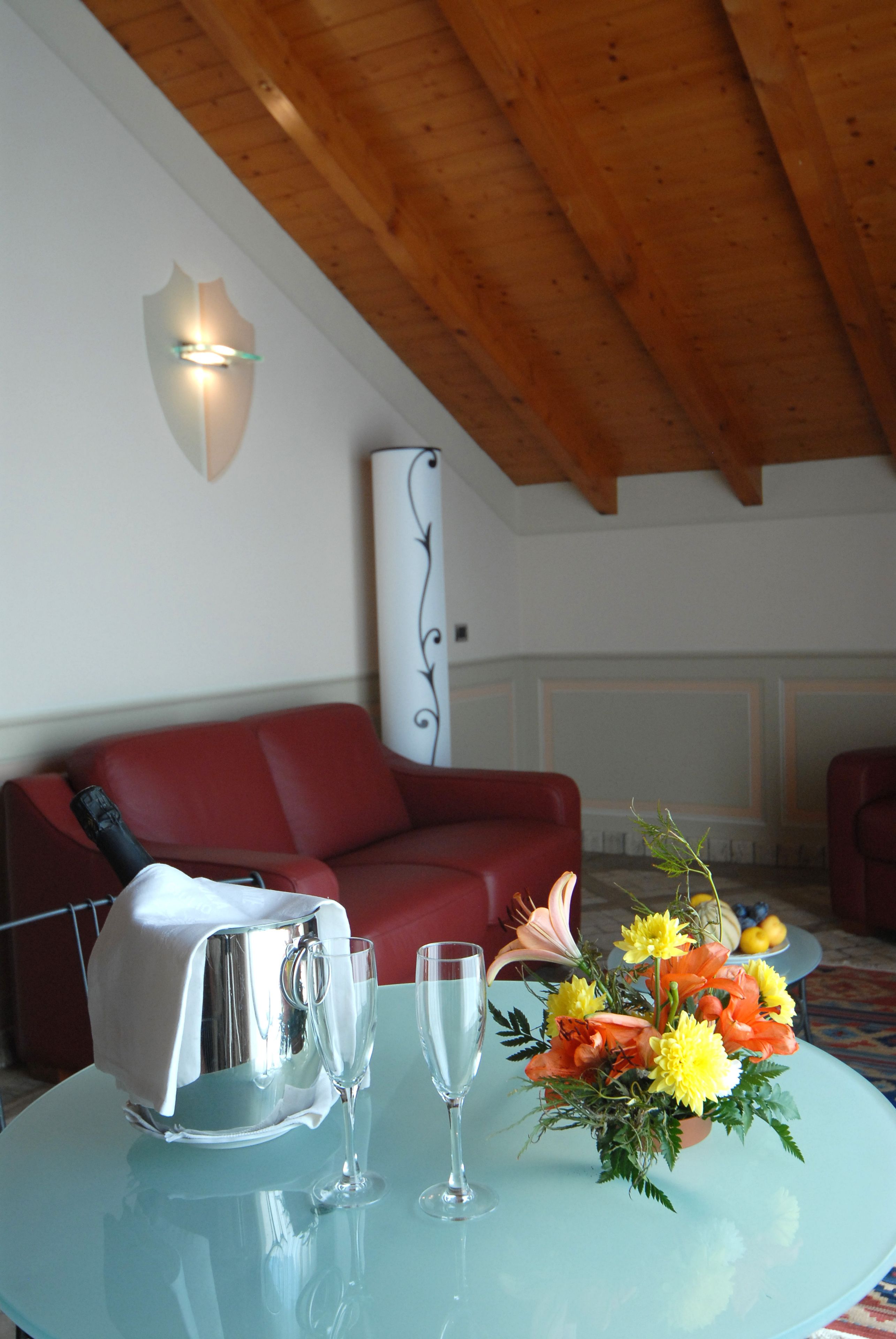 A room with a red sofa, a glass table with a bottle and glasses, and a floral arrangement.