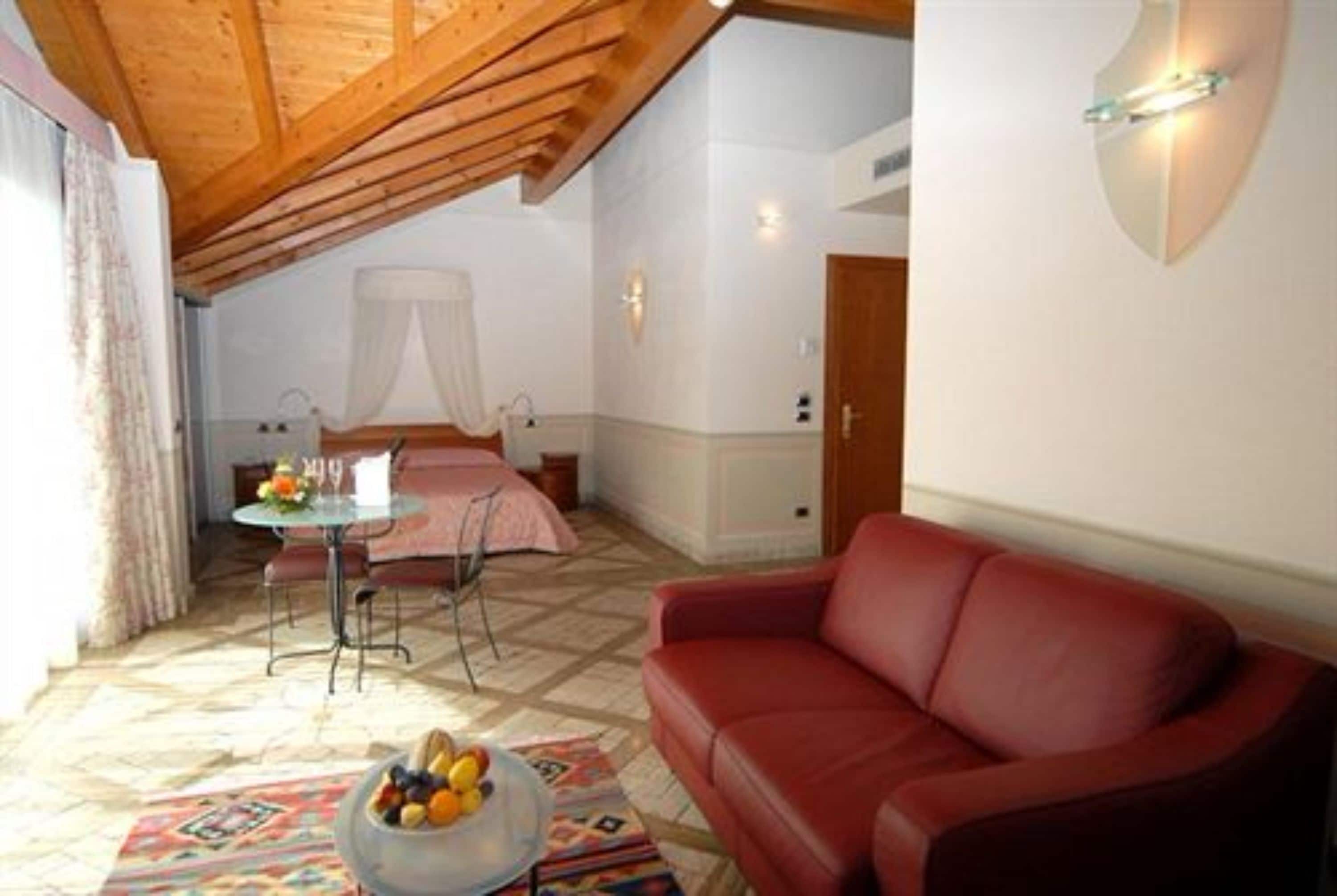 A cozy room with a red sofa, a small table with fruit, a bed with a canopy, and a wooden ceiling.