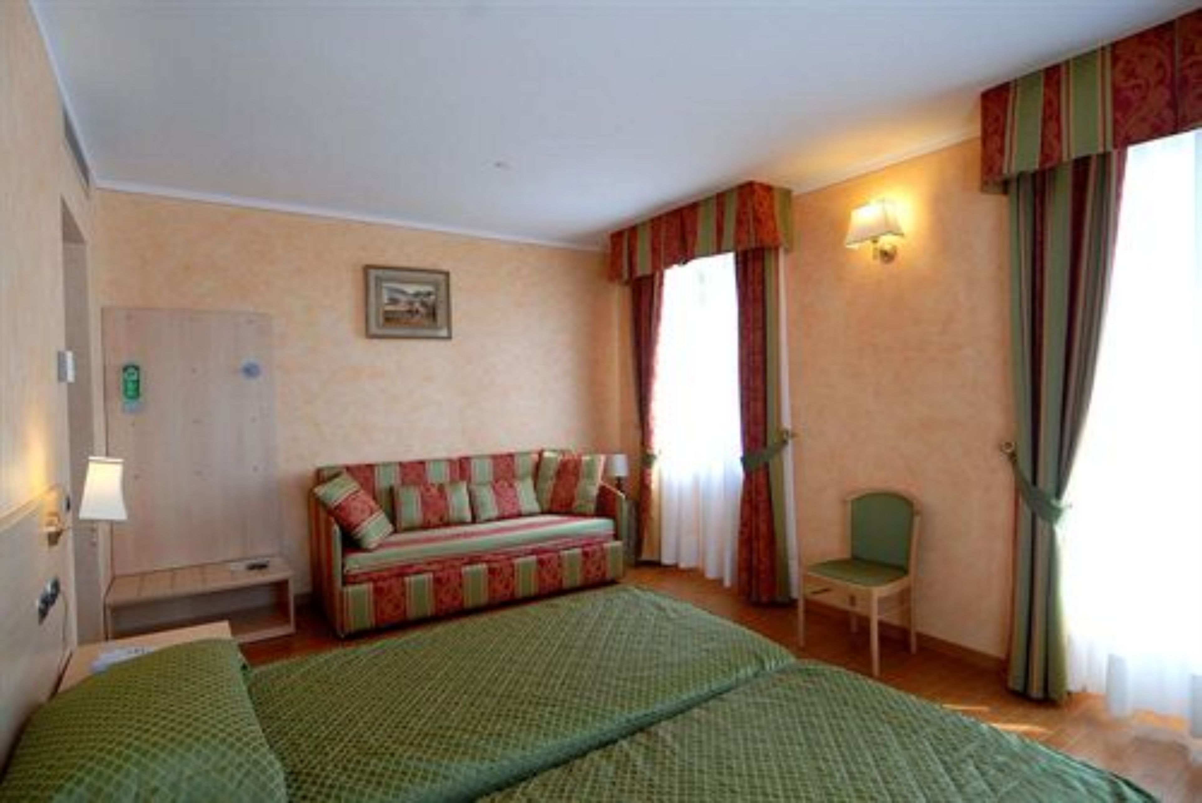 A hotel room with a bed, a sofa, a chair, a desk, a lamp, a picture on the wall, and a window with curtains.