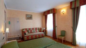 Une chambre d’hôtel avec un lit, un canapé, une chaise, un bureau, une lampe, un tableau au mur et une fenêtre avec des rideaux.