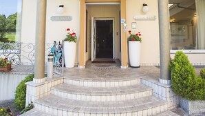 L’entrée de l’hôtel La Bussola se distingue par sa façade incurvée, un escalier menant à l’entrée et des plantes en pot de chaque côté.