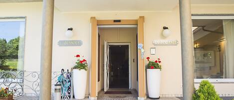 La entrada del hotel La Bussola, con una fachada curva, una escalera que conduce a la entrada y plantas en macetas a ambos lados.