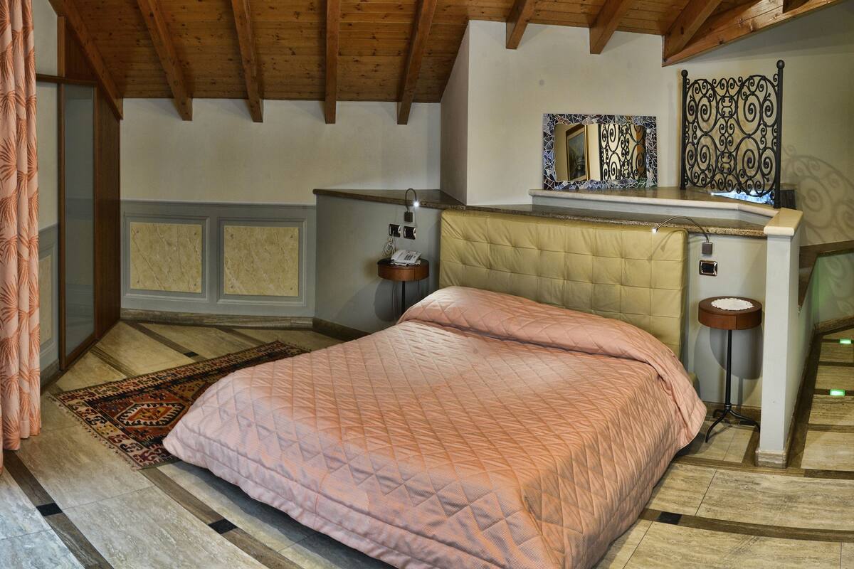 Een slaapkamer met een bed, een raam met gordijnen, een nachtkastje en een spiegel.