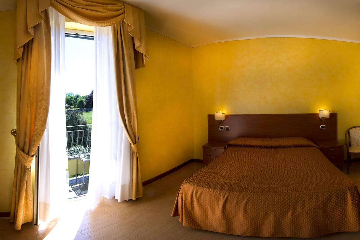 Een hotelkamer met een bed, nachtkastjes, een lamp en uitzicht op het buiten.