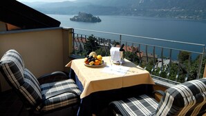 Un balcon avec une table dressée pour deux personnes, donnant sur un lac avec une petite île et des montagnes à l’horizon.