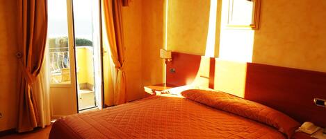 Habitación de hotel con una cama, mesita de noche, lámpara y vistas por la ventana.