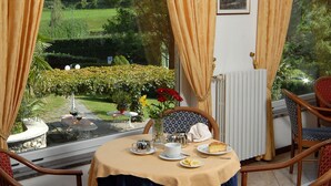Un coin repas avec une table dressée pour deux personnes, un radiateur et une vue sur un jardin.
