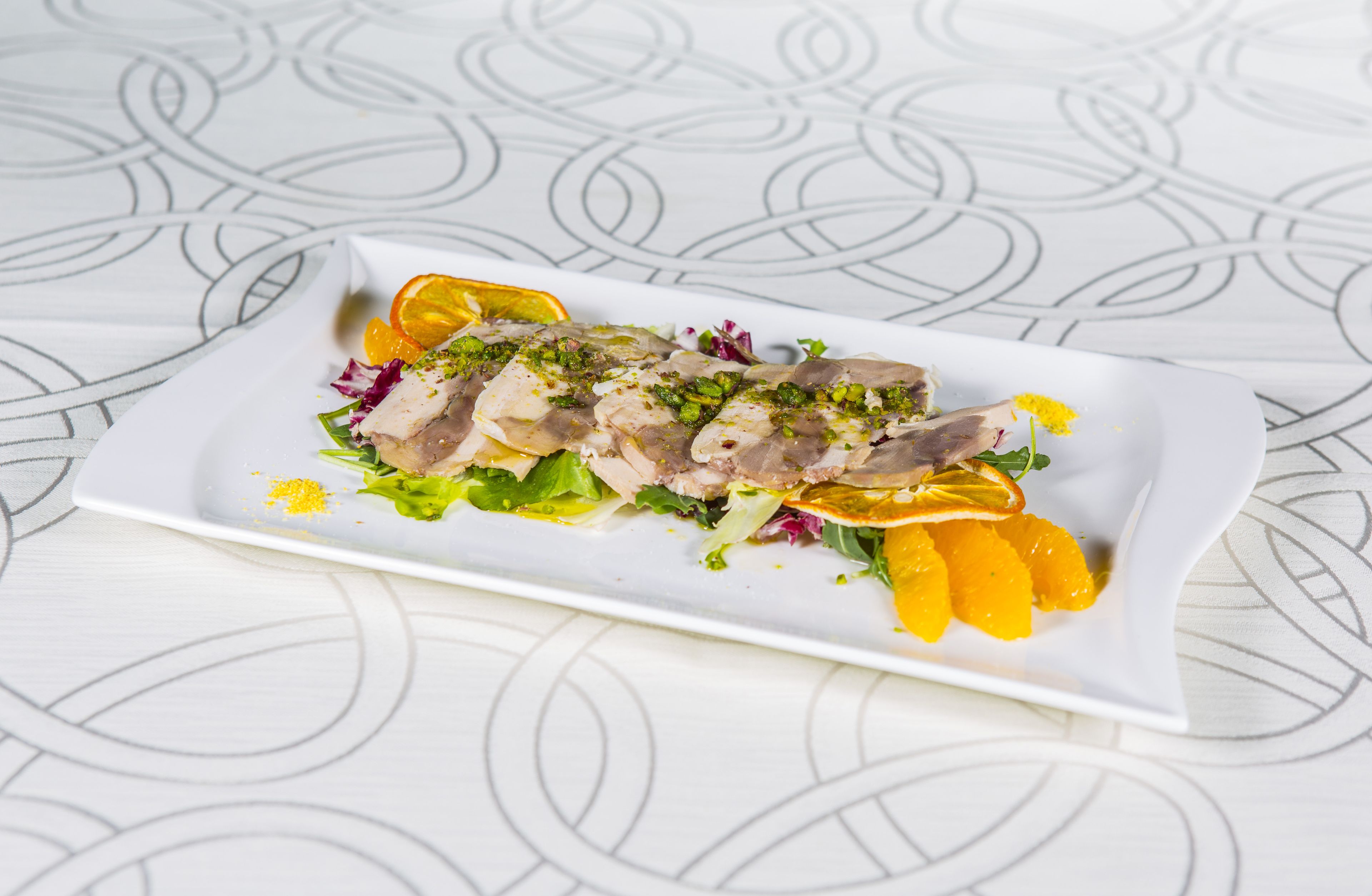 Plato blanco rectangular con un plato de mariscos, adornado con hierbas y segmentos de naranja, sobre una mesa con un diseño geométrico.