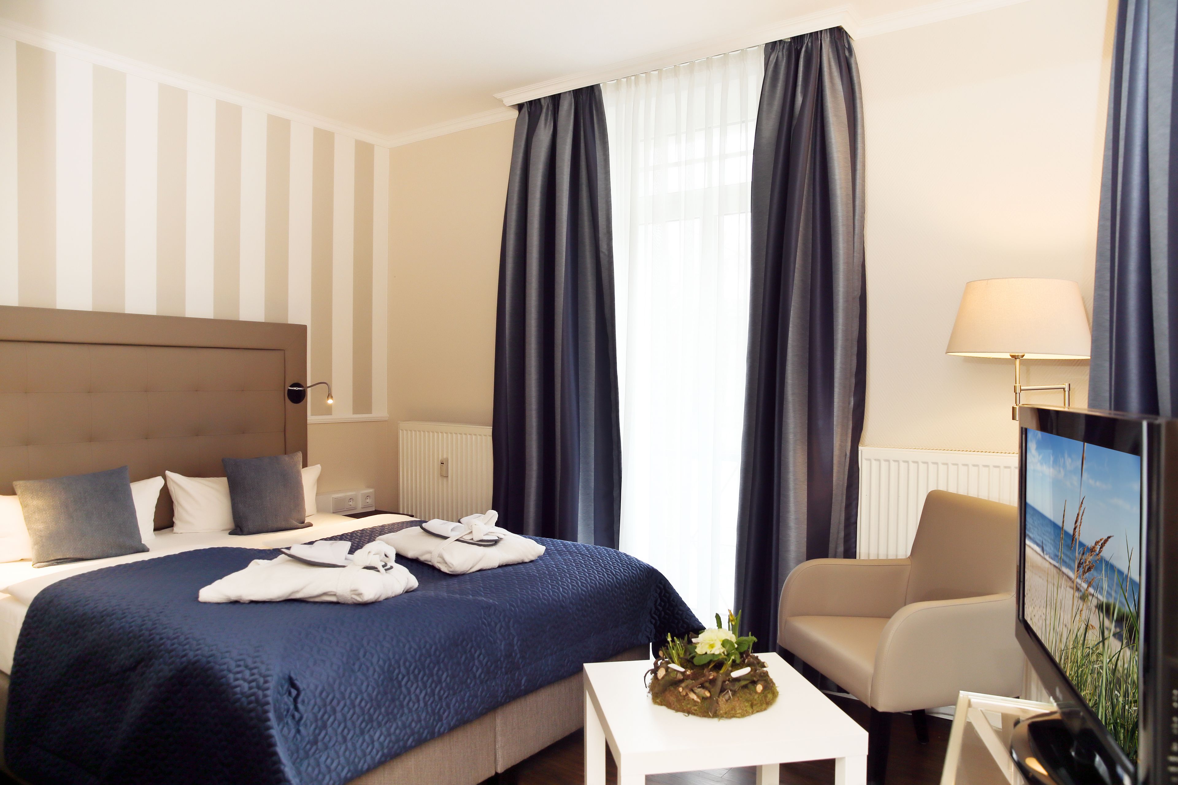 Habitación de hotel con una cama grande, un televisor de pantalla plana, una silla y una mesa con una planta.