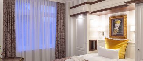 Una habitación de hotel con cama, una silla, un cuadro enmarcado y una ventana con cortinas.