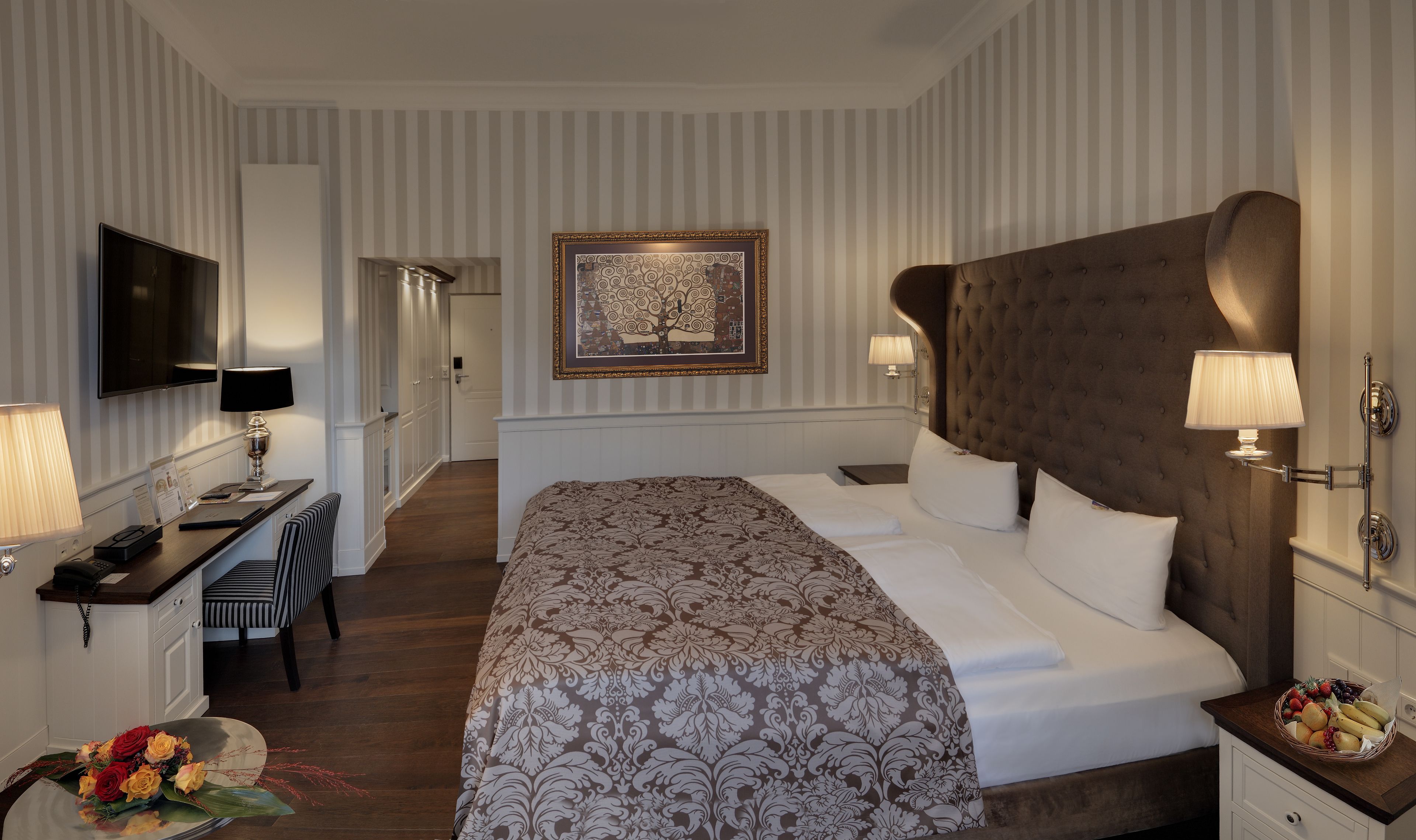 Habitación de hotel con una cama grande, un escritorio con silla, un televisor y un cuadro en la pared.