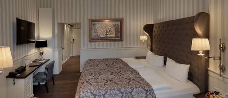 Habitación de hotel con una cama grande, un escritorio con silla, un televisor y un cuadro en la pared.