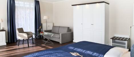 A hotel room with a bed, a desk, a chair, a sofa, and a wardrobe.