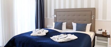 Una cama bien hecha con colcha azul oscuro, almohadas blancas y cabecera gris. Hay dos juegos de toallas blancas sobre la cama.