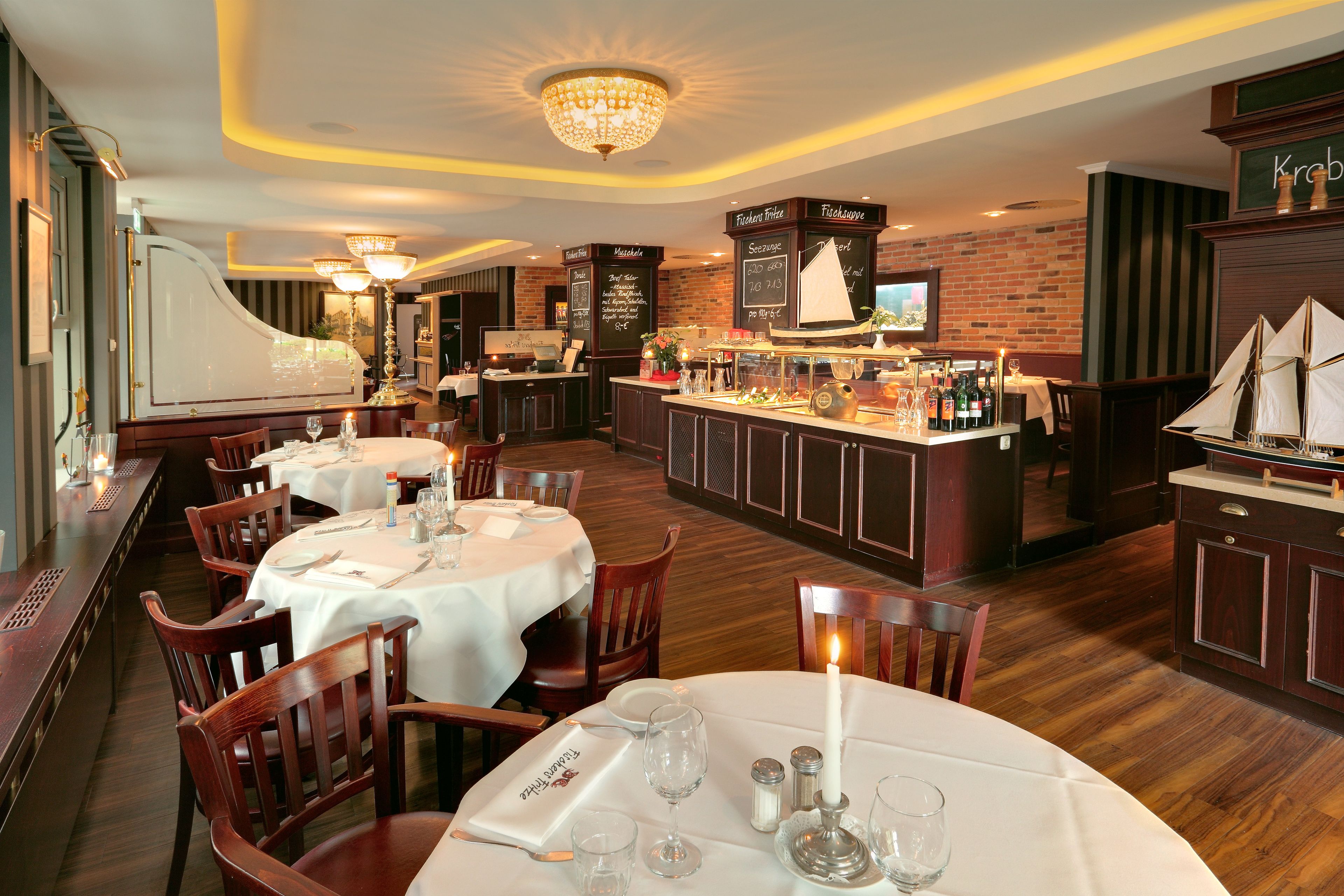 A restaurant with round tables, wooden chairs, a bar area, and a chandelier.