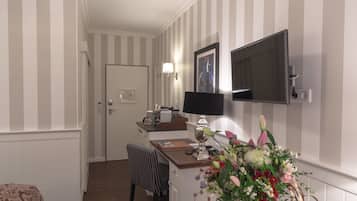 Habitación de hotel con una pared a rayas, un televisor de pantalla plana sobre un escritorio de madera, una silla y un arreglo floral en el escritorio.