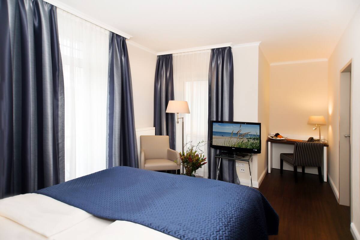Habitación de hotel con cama, escritorio, silla, televisión y lámpara.