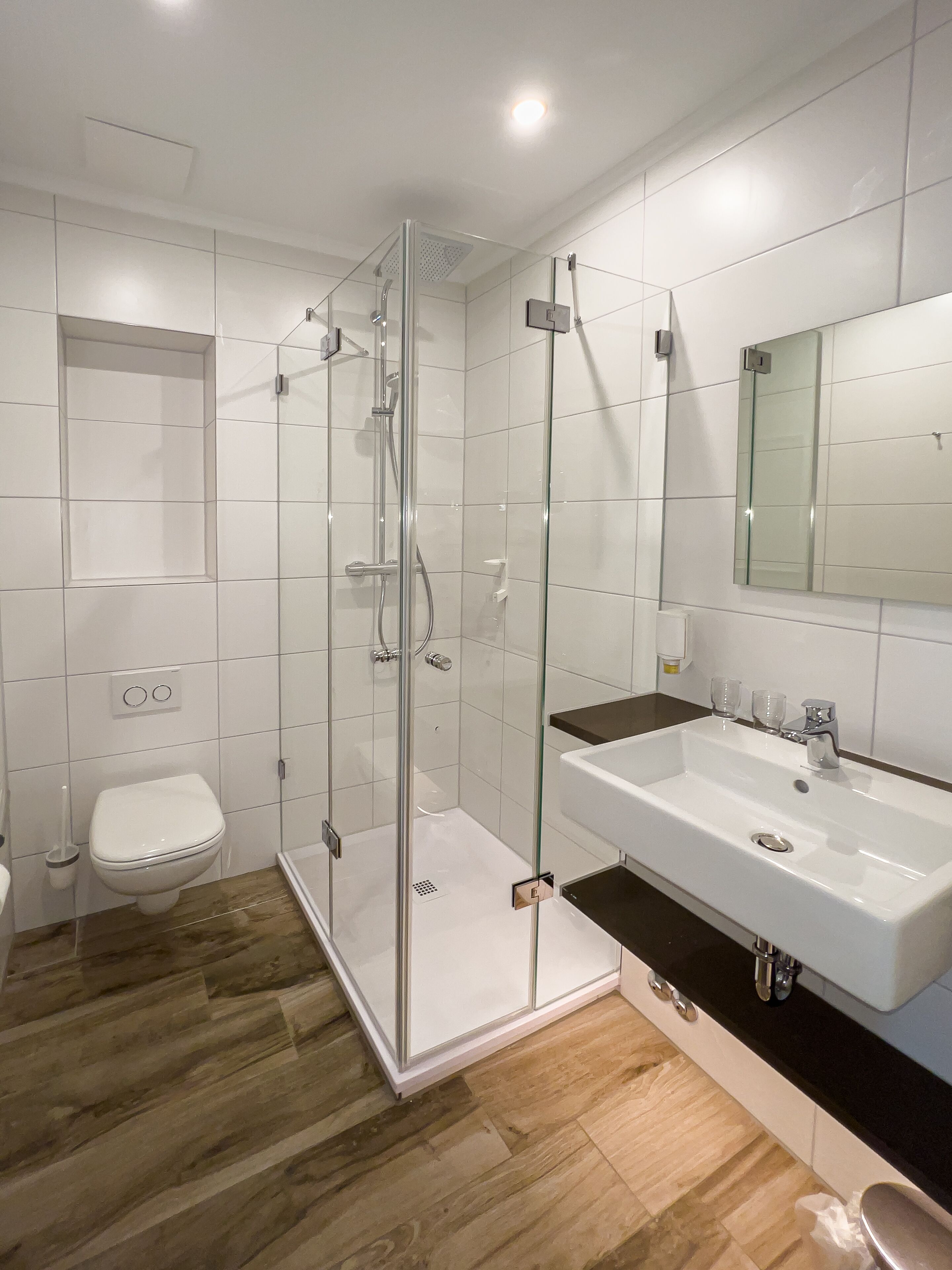 Un baño moderno con ducha envuelta en vidrio, un lavamanos blanco y un espejo grande.