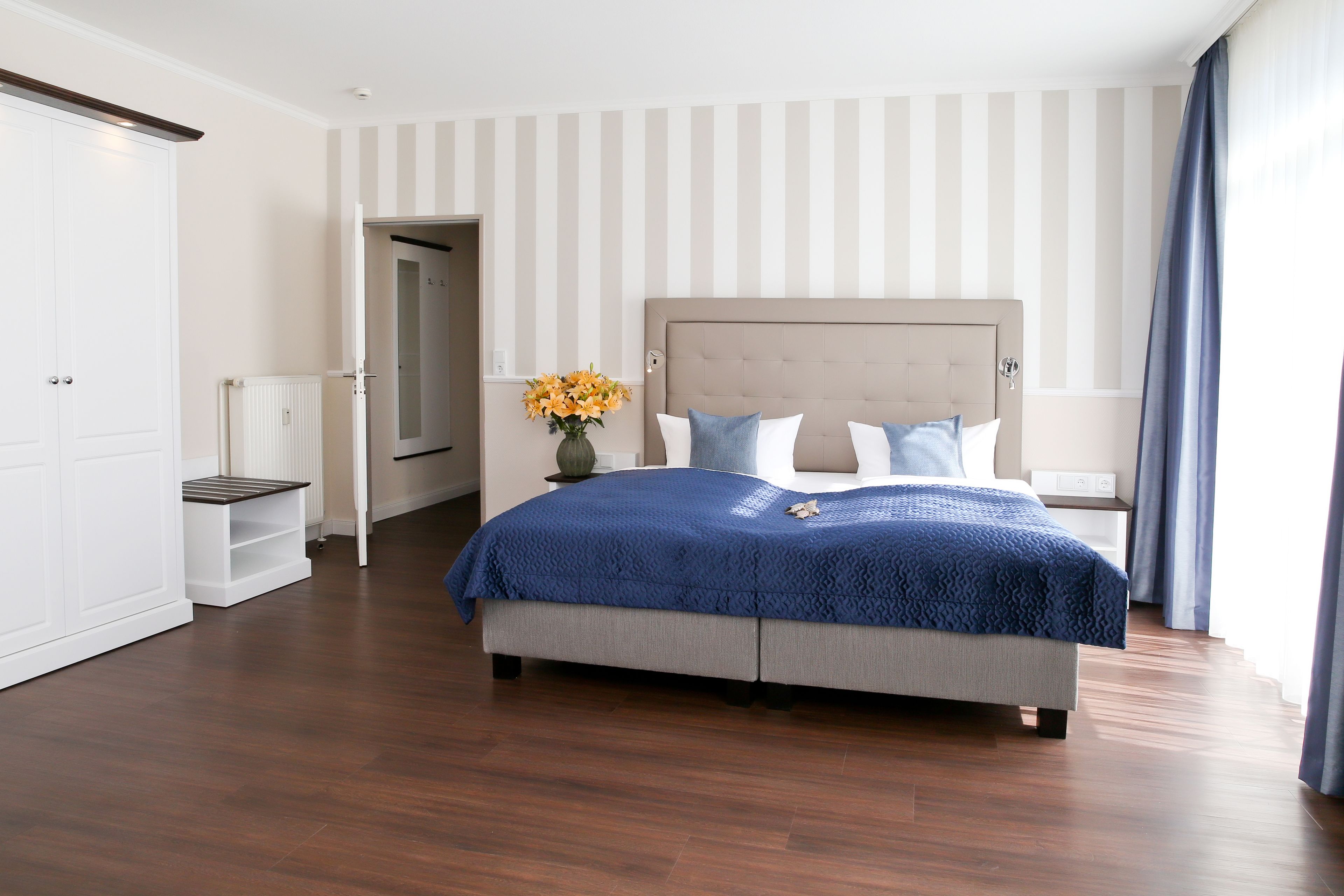 Ein Schlafzimmer mit einem großen Bett, einem Nachttisch, einem Kleiderschrank und einer Vase mit Blumen.