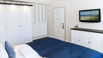 A bedroom with a bed, white wardrobes, a television on the wall, and a beach scene on the screen.