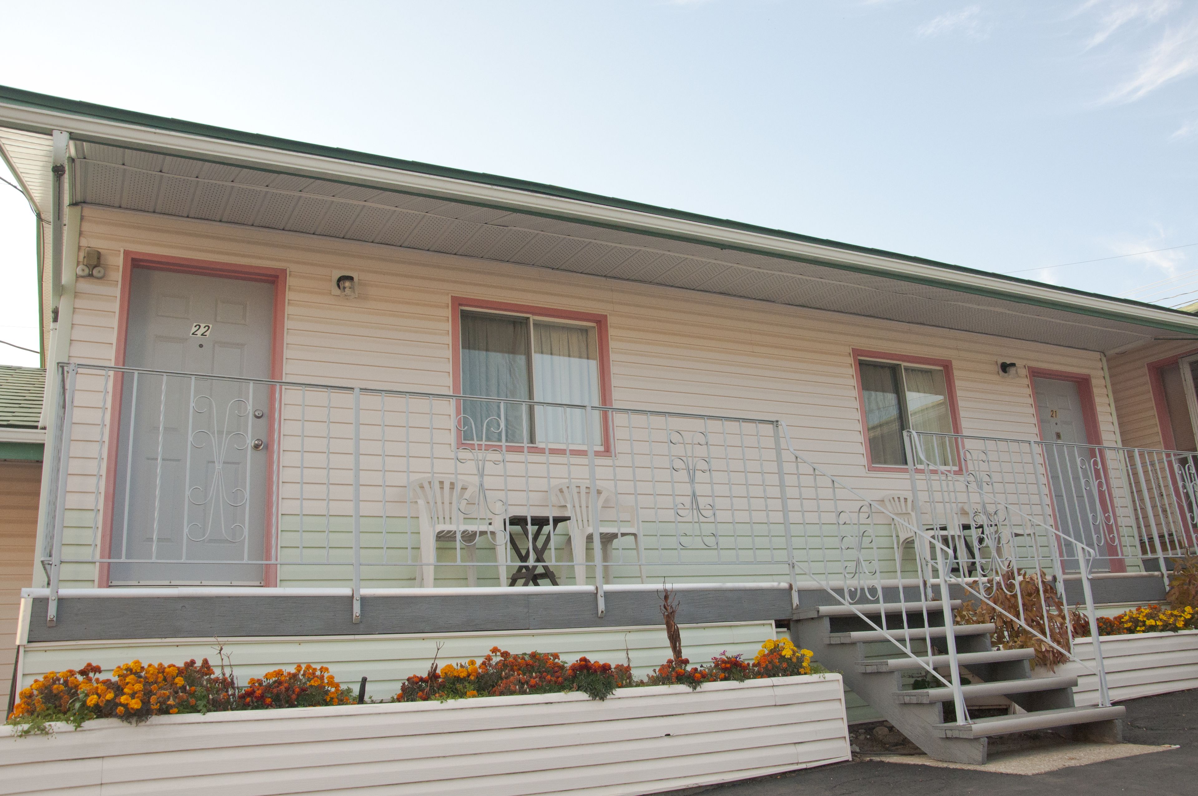Een gelijkvloers motel met een veranda, een kleine tafel en stoelen, en een trap naar de ingang.