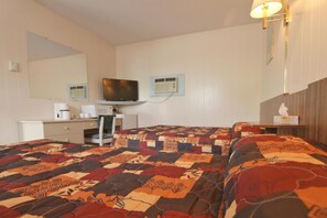 A hotel room with a bed, a desk, a television, and a bedside table with a lamp.