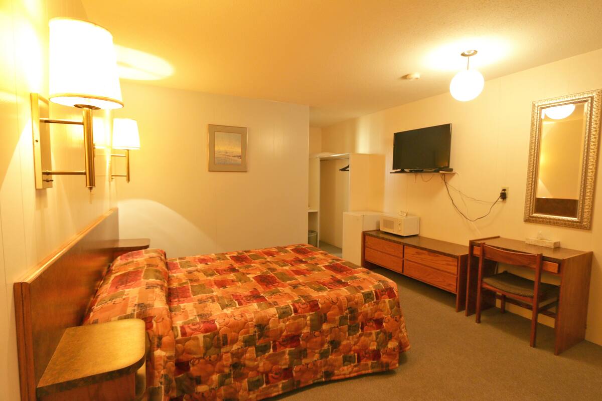 Una habitación de hotel con una cama, un escritorio, una silla, un televisor y un espejo.