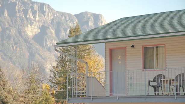 Un motel doté d’un toit végétalisé, d’une porte rouge et d’un balcon avec des chaises.