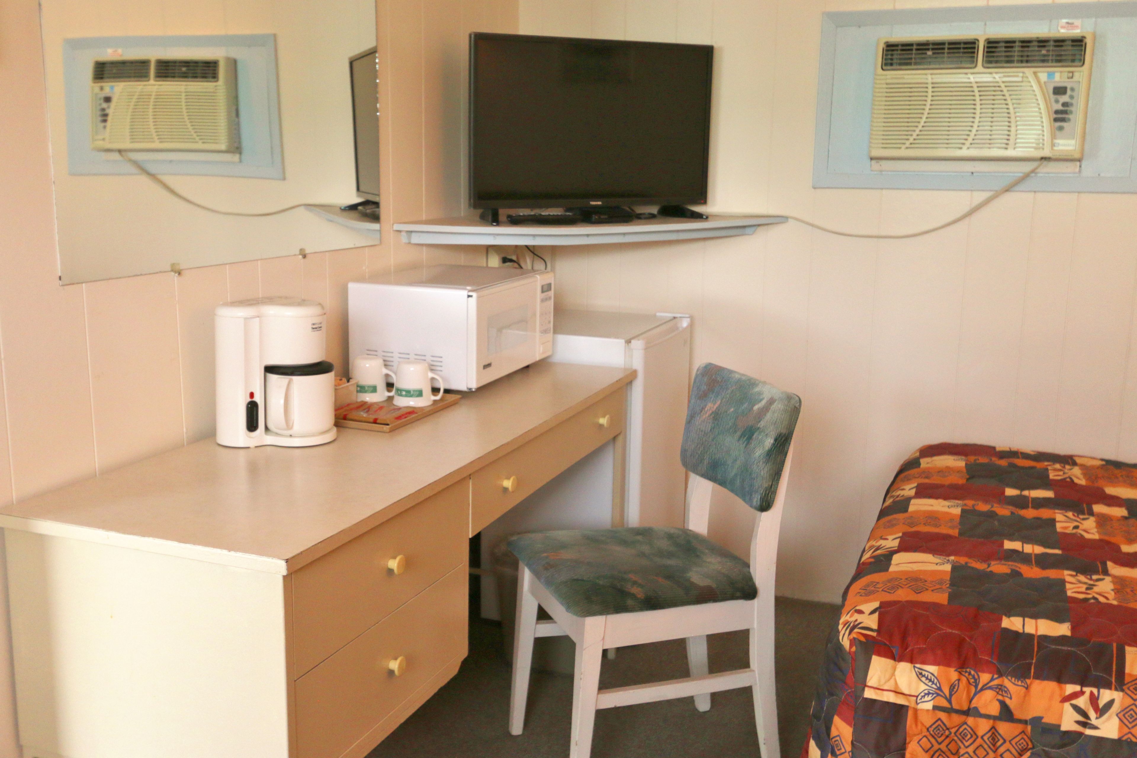 A hotel room with a bed, a desk with a computer, a chair, a television, and two air conditioning units.