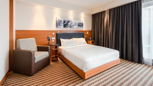 A hotel room with a large bed, a chair, a nightstand, and a wall-mounted artwork. - Hampton by Hilton Warsaw Airport (Warsaw)