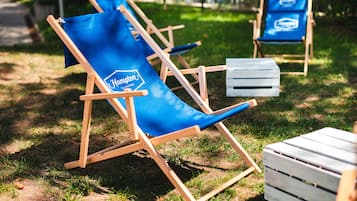 A row of blue lounge chairs with wooden frames and a white bench, set on a grassy area.