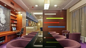 A modern hotel lobby with a long reception desk, purple seating, a bookshelf, and a decorative wall with horizontal lines. - Hampton by Hilton Warsaw Airport (Warsaw)