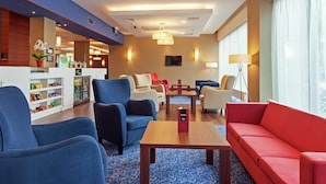 A hotel lobby with seating areas, a reception desk, and a television. - Hampton by Hilton Warsaw Airport (Warsaw)
